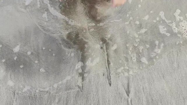 Video clip of a person drawing on the beach sand with waves