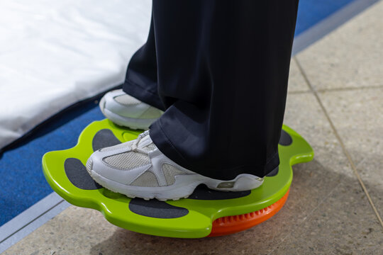 Person Standing on a Green Balance Board. Person wearing white sneakers stands on a green balance board during indoor exercise.