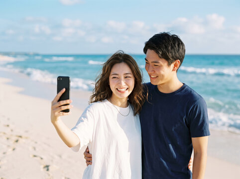 明るい日差しのビーチで携帯電話を構えて自撮りする仲睦まじいカップルと女性