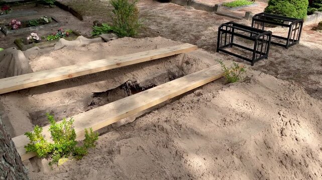 Fresh open grave prepared for burial in a peaceful cemetery in Latvia with coffin stands, wooden support planks and sandy soil before the funeral ceremony begins