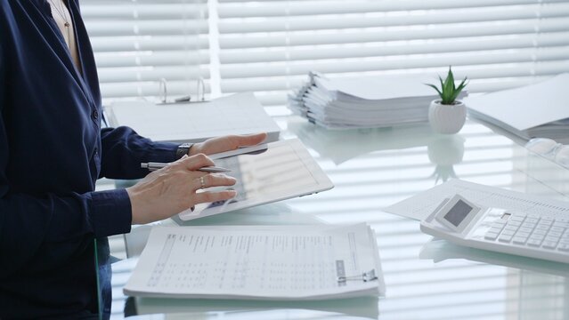 Professional woman using digital tablet for business tasks, typing data and reviewing documents at a modern office desk, symbolizing efficiency and financial management