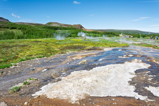 Icelandic geothermal area showcasing steam rising from hot springs and boiling water flowing over mineral deposits on the colorful ground under a clear blue sky
