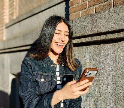 Portrait of a happy young woman tourist travelling or student or a businesswoman entrepreneur, using a smartphone phone or texting outdoors in front of a modern urban background