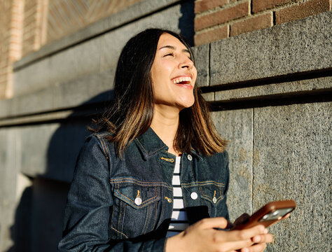 Portrait of a happy young woman tourist travelling or student or a businesswoman entrepreneur, using a smartphone phone or texting outdoors in front of a modern urban background