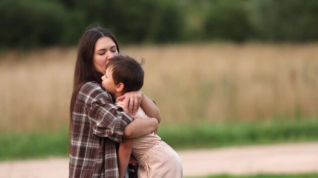 Slow motion shows mother hugging and kissing her autistic son on cheek in nature. Boy remains distressed despite her comfort. Emotional scene reflects patience support and unconditional love.