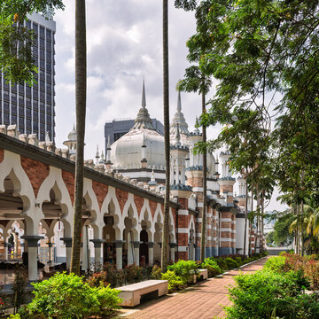 View of the historic Jamek Mosque featuring iconic Moorish architecture, white domes, and arched walkways surrounded by palm trees in the city center in Kuala Lumpur, Malaysia