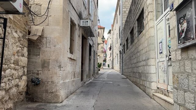 Split, Croatia - October 07, 2025: Narrow cobblestone alleyway transitions into a quaint courtyard with outdoor seating and a visible restaurant in a charming Mediterranean town