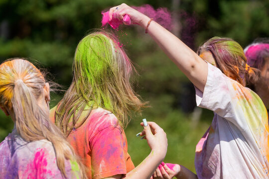 People throwing pink and green powder outdoors at a color festival, hair covered in bright paint. Fun summer holiday, celebration. holi festival