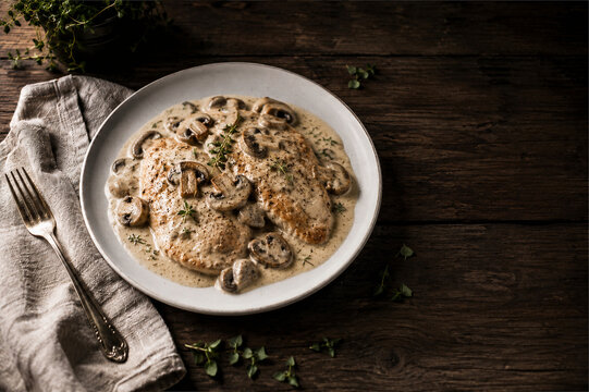 Delicious chicken breasts in a rich creamy mushroom sauce garnished with fresh thyme on a rustic wooden table