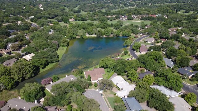 Algae rich retention waters stretch beside Pebble Beach Dr residences in Austin suburban developments. Quiet street cul de sacs terminate near scenic neighborhood ponds, Travis County, Texas