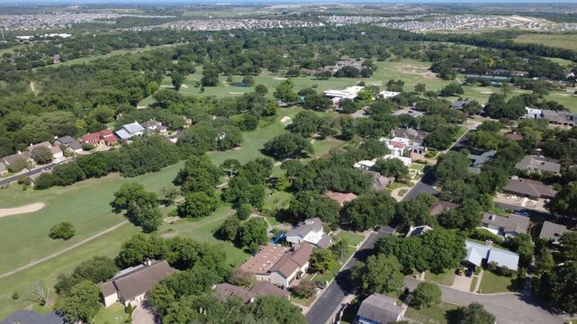 Manicured golf fairways extend beside single family home yards near Pebble Beach Drive in Austin suburban corridors. Oak canopies shade quiet residential streets across broader region developments