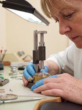 watchmaker redhead woman press case technician safety repair workshop precision redhead craftswoman operates a bench press on a watch case wearing blue finger guards for safe luxury assembly