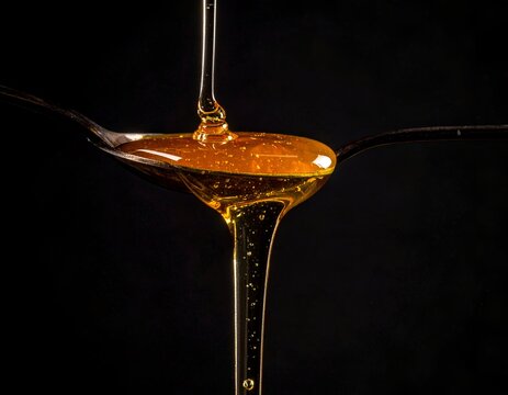 Golden clear honey dripping from a spoon over delicious grilled food skewers against a dark moody background