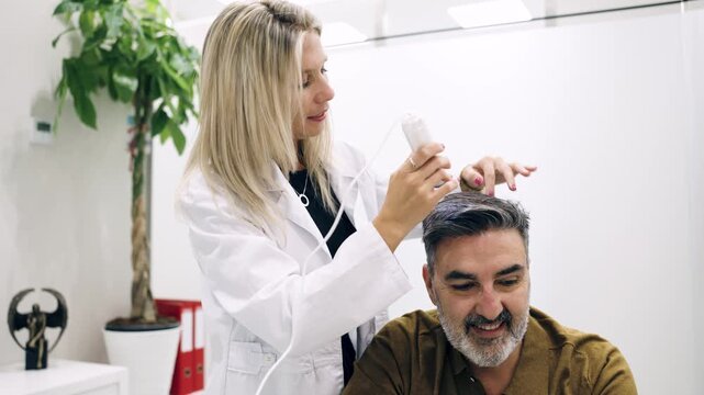 Female trichologist using a trichoscope to diagnose a male patient's hair and scalp condition. Modern cosmetic clinic providing hair loss treatment