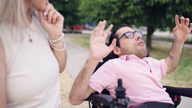 Man with a physical disability having an epileptic seizure in his electric wheelchair while a woman tries to help him outdoors in a park