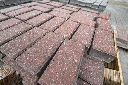 Red pavers are neatly arranged and stacked on a wooden pallet at a construction site. Materials are ready for upcoming projects during the day