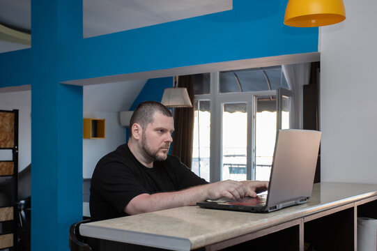 male freelancer types on a computer in a bright apartment, showing independent digital work, online communication and a flexible work from home routine in a modern interior