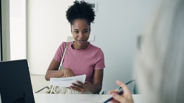 Young black woman checking in at a clinic, talking to the receptionist and signing a medical form before a doctor's appointment