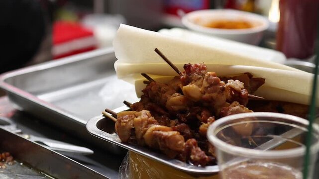 Grilled chicken skewers with paper wrapping served on metal tray at Asian street food market stall. Close up of traditional meat kebabs on wooden sticks, local fast food and travel concept.