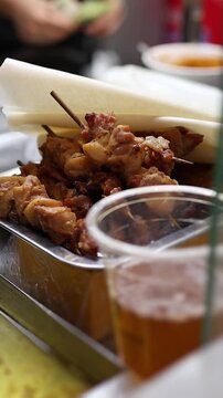 Grilled chicken skewers with paper wrapping served on metal tray at Asian street food market stall. Close up of traditional meat kebabs on wooden sticks, local fast food and travel concept.