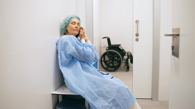Anxious senior woman wearing a surgical gown and cap while waiting for her operation. A wheelchair is visible in the background