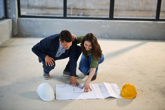 Young happy couple communicating while analyzing housing plans at construction site.