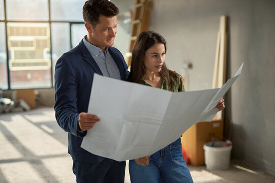 Young couple looking at blueprints together during house renovation in apartment