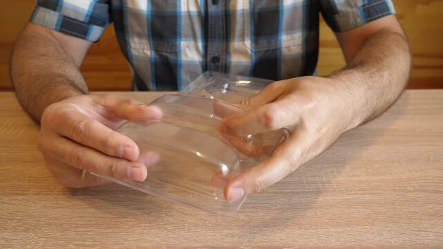 A man crumples clear plastic packaging in his hands, creating a distinctive crackling sound while bending it. The video contains clean original audio.