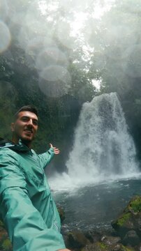 Young male content creator filming himself with a beautiful waterfall in the background at Arenal Volcano National Park, Costa Rica