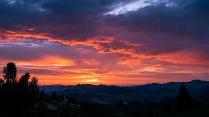 Obraz premium A dramatic sunset sky painted in fiery reds and purples above rolling hills and silhouetted trees