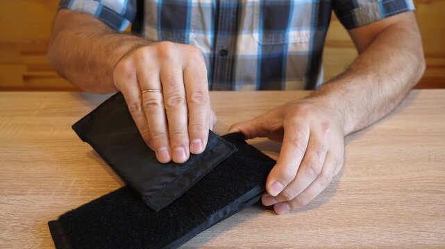 A man separates and fastens a fabric hook and loop fastener, creating a distinctive ripping sound. The video contains clean original audio.