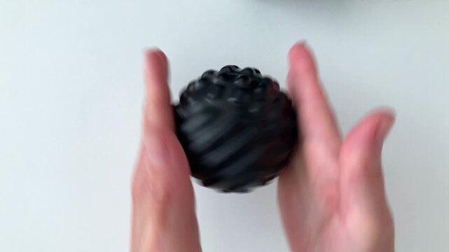 A woman with a black massage ball rolls a ball between her palms, does hand exercises. Top view of women's palms. Preventing fatigue during prolonged arm strain