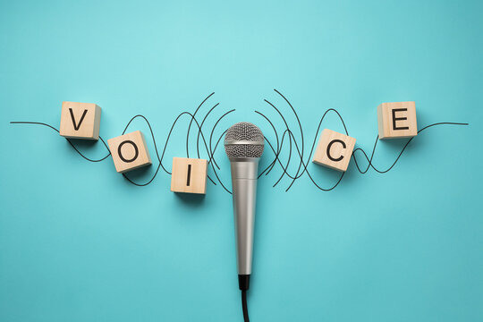 Voice concept with a microphone and wooden blocks spelling out the word on a blue background