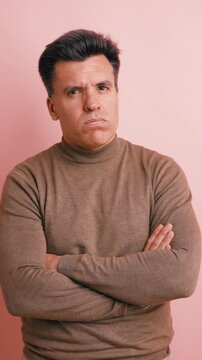 Serious middle aged man with arms crossed expressing doubt and mistrust. Portrait of a suspicious person on a pink background. Vertical