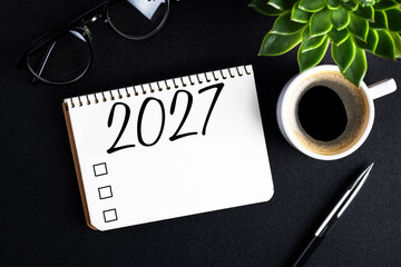 Naklejka premium 2027 New year resolutions on desk. 2027 goals list with notebook, coffee cup, plant on black table. Resolutions, plan, goals, action, checklist, idea concept. New Year 2027 resolutions. Copy space