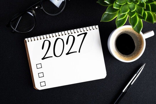 2027 New year resolutions on desk. 2027 goals list with notebook, coffee cup, plant on black table. Resolutions, plan, goals, action, checklist, idea concept. New Year 2027 resolutions. Copy space