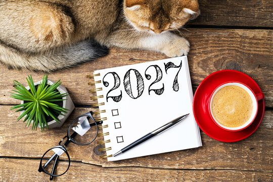 New year resolutions 2027 on desk. 2027 resolutions list with notebook, coffee cup, cute cat on table. Goals, resolutions, plan, cozy, hygge concept. New Year 2027 template, copy space
