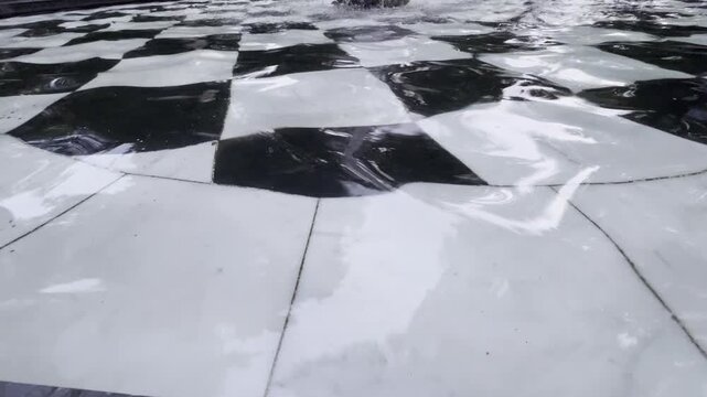 Rippling water in a fountain basin with a black and white checkered bottom in the Summer Garden. Abstract pattern of moving water, reflections and geometric shapes creating a decorative texture.