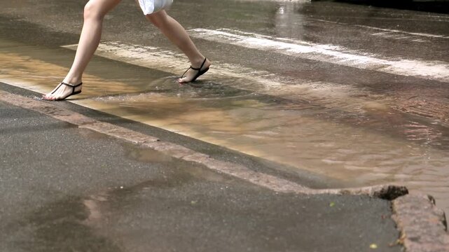 Low angle view of female legs in sandals stepping through a deep puddle on a flooded crosswalk in the city after a heavy downpour