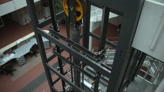 Elevator shaft interior with steel guide rails, cables, pulley system, and recessed cylinder seen from high oblique angle inside industrial structure, with elevator, shaft, cable, rail detail