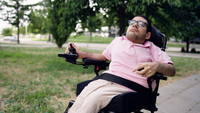 Man with a physical disability using a joystick to operate a powered wheelchair outdoors, representing mobility and autonomy