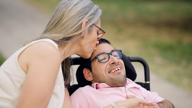 Mother showing love and affection by kissing her adult son with physical disability on his forehead, highlighting family care