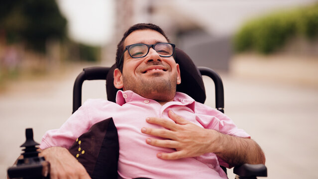 Man with spina bifida experiencing joy and happiness, sitting in his powered wheelchair outdoors