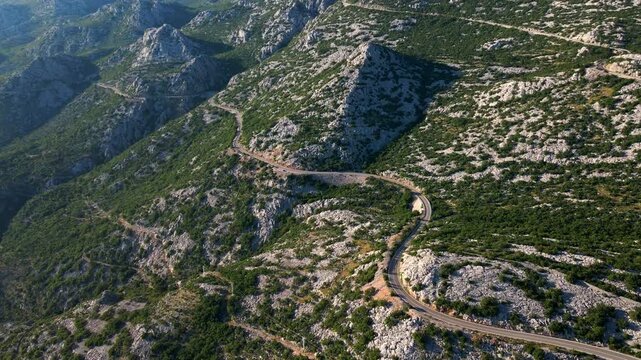 Empty winding mountain road through rugged rocky landscape from above