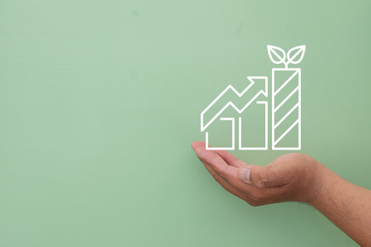 Sustainable business growth and green investment concept. Hand holding a digital financial chart graphic with leaves against a light green background with copy space.