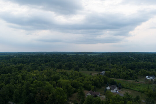 Aerial view of lush green forests and distant rural homes under a cloudy sky
