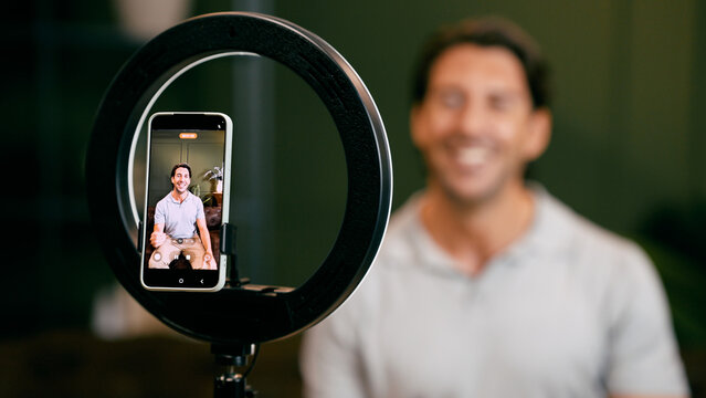 Man creating digital content, recording a podcast or video with a smartphone and ring light, engaging with his audience