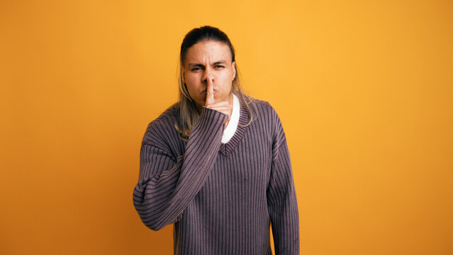 Latino man with long hair making a shhh gesture, expressing quietness, secrecy, and privacy in a studio setting