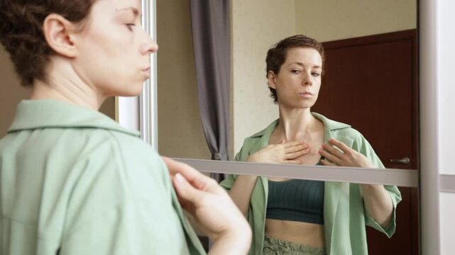 woman glances down at the chest port in a bedroom mirror, capturing a private moment of self care, sensitivity and adjustment to daily life during cancer recovery