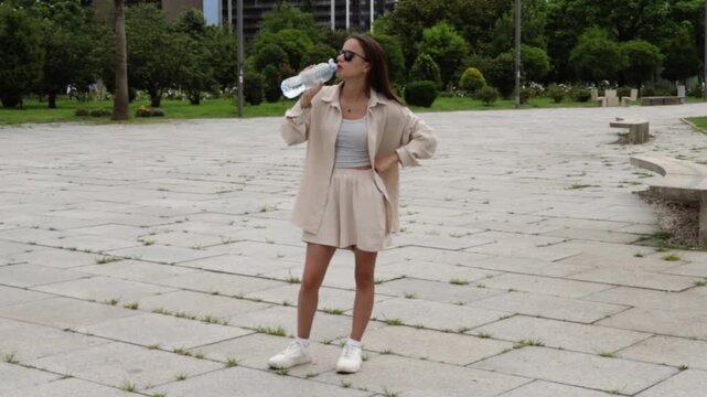 teenager drinks water outdoors in a modern residential district, demonstrating daily hydration and heat protection during a hot urban summer day